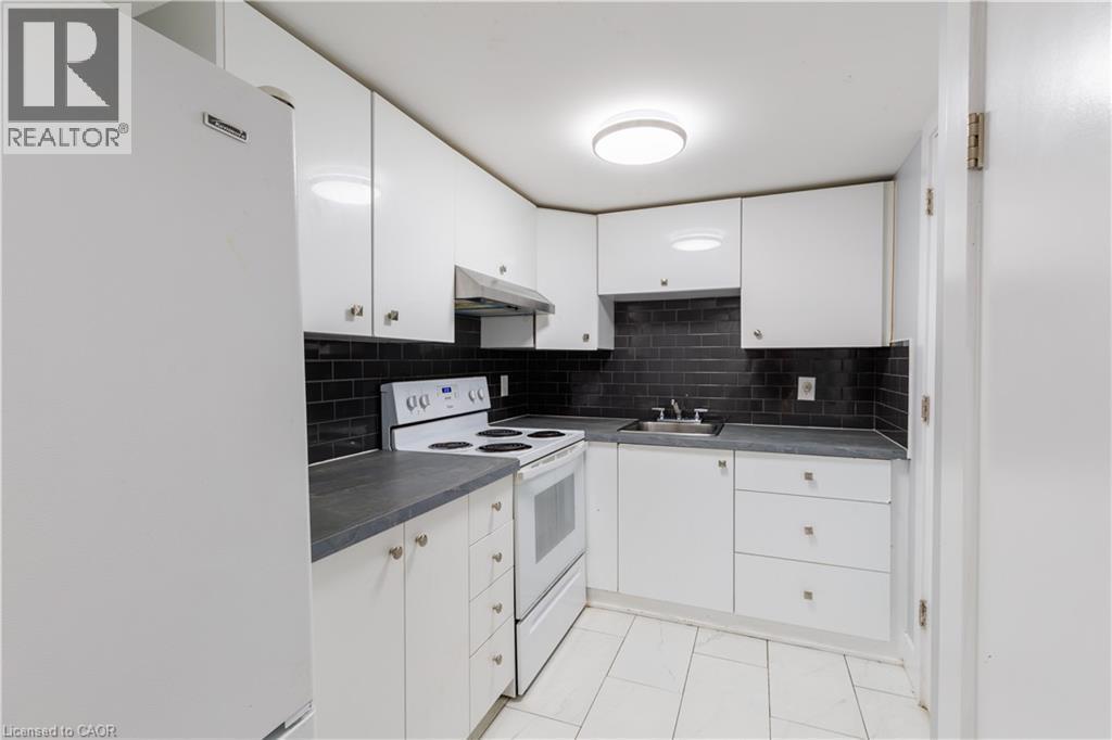 Kitchen featuring white cabinetry, dark countertops, white appliances, a dark subway tile backsplash, and white tile flooring - 18 Silverdale Crescent, London, ON - Indoor Photo Showing Kitchen
