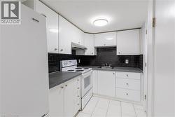 Kitchen featuring white cabinetry, dark countertops, white appliances, a dark subway tile backsplash, and white tile flooring -