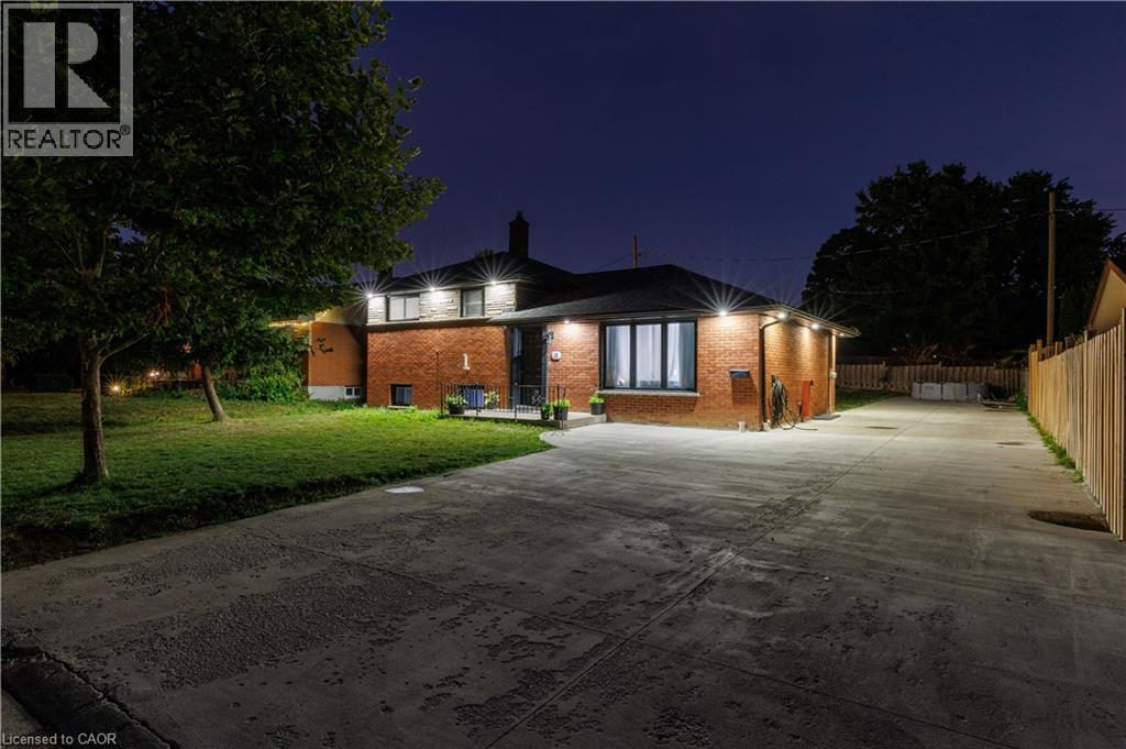 Brick exterior residence featuring a concrete driveway, established trees, a fenced side yard, and exterior lighting fixtures - 18 Silverdale Crescent, London, ON - Outdoor
