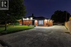 Brick exterior residence featuring a concrete driveway, established trees, a fenced side yard, and exterior lighting fixtures -