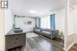 Spacious living area featuring wood-finish flooring, white walls, and a large window with sheers -