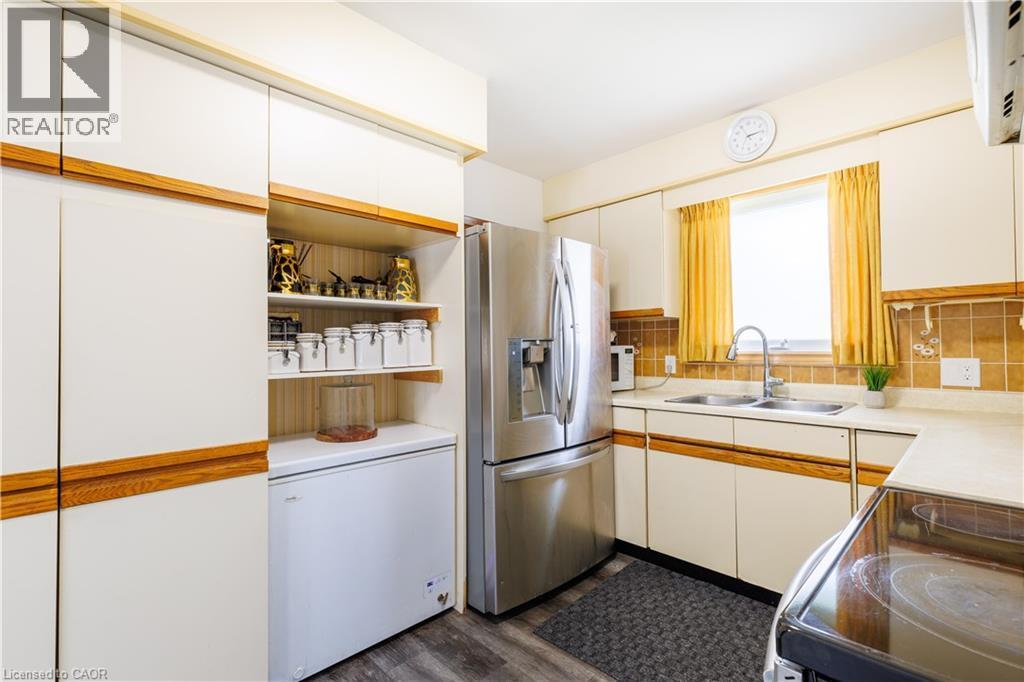 Kitchen featuring light-toned cabinetry with wood-finish accents, stainless steel refrigerator, and a double basin sink with a gooseneck faucet - 18 Silverdale Crescent, London, ON - Indoor Photo Showing Kitchen With Double Sink