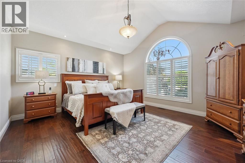 Vaulted ceiling bedroom featuring dark wood-finish flooring, recessed lighting, and a large arched window with plantation shutters - 20 Bonniewood Drive, Drayton, ON - Indoor Photo Showing Bedroom
