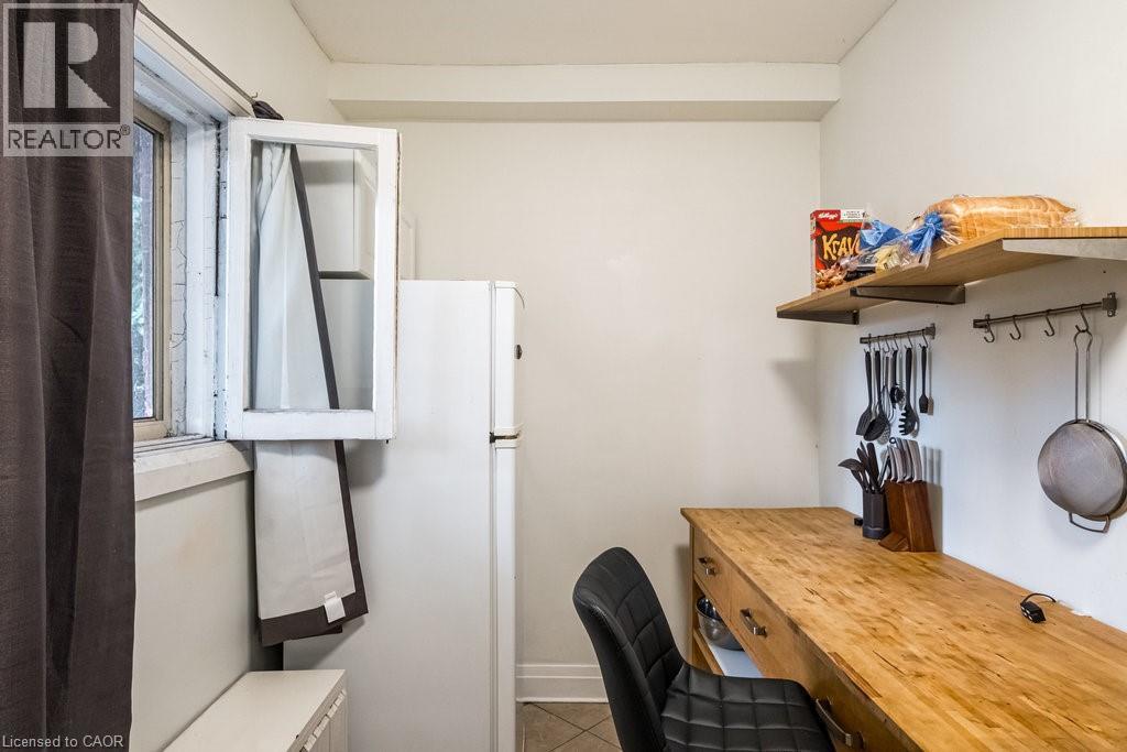 Compact kitchen area featuring a white refrigerator and a window with an open-faced cabinet - 95-97 S Fairholt Road S, Hamilton, ON - Indoor