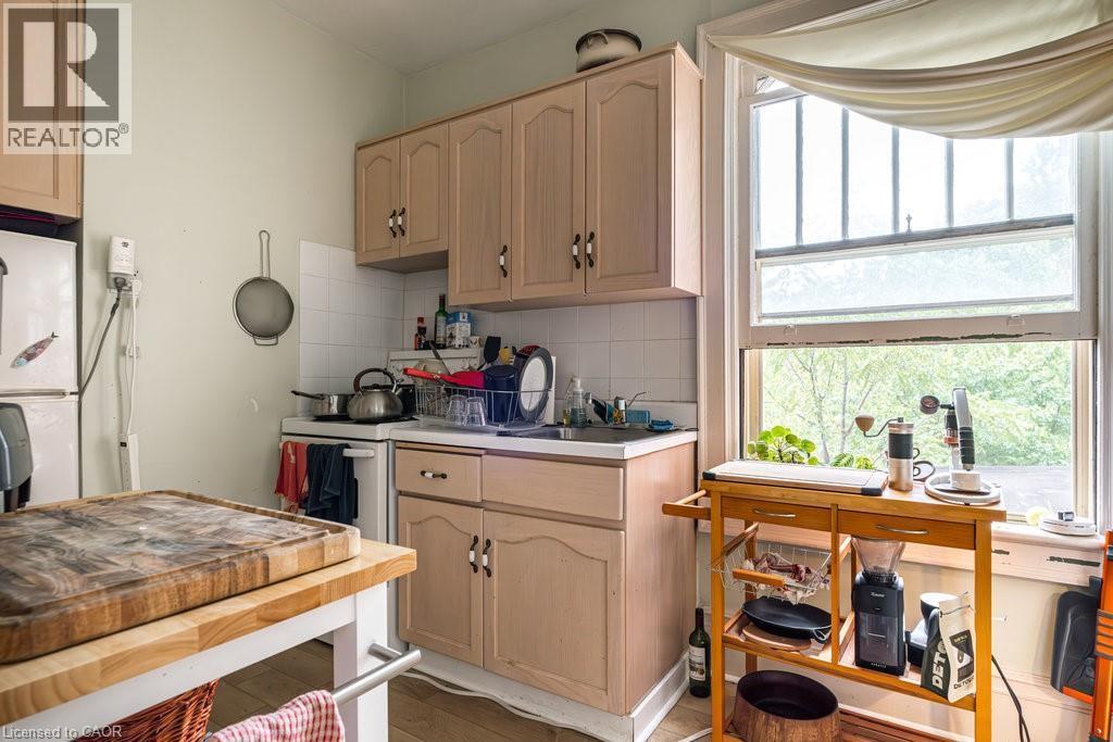 Kitchen featuring neutral-toned cabinetry, a white tile backsplash, and a window with a wooded backdrop - 95-97 S Fairholt Road S, Hamilton, ON - Indoor Photo Showing Kitchen