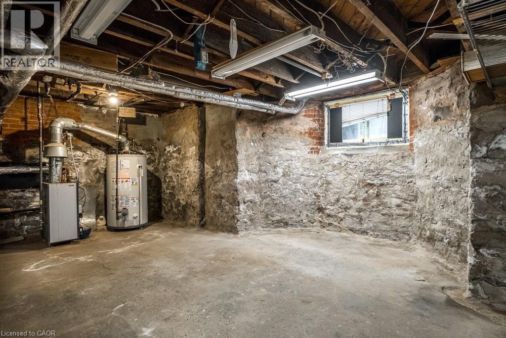 Basement utility area featuring a hot water heater, furnace, concrete flooring, exposed stone foundation walls, and a window - 95-97 S Fairholt Road S, Hamilton, ON - Indoor Photo Showing Basement