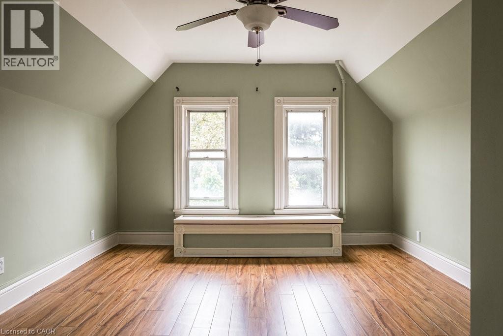 Room featuring wood-finish flooring, two sash windows with detailed trim, a built-in window bench, a ceiling fan, and sloped ceilings - 95-97 S Fairholt Road S, Hamilton, ON - Indoor Photo Showing Other Room