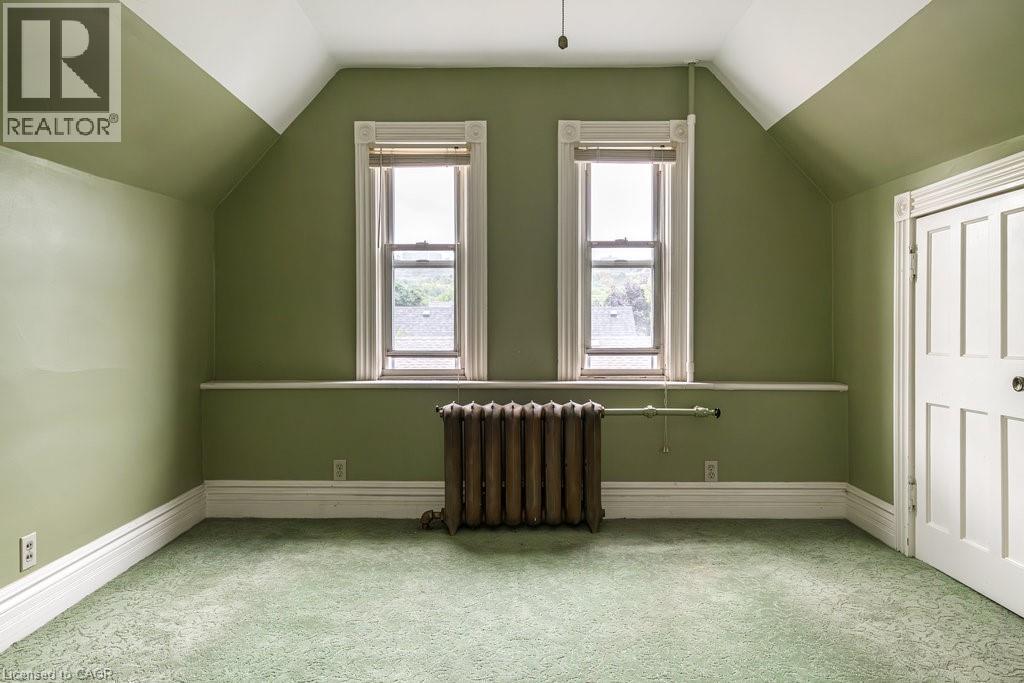 Room featuring dual windows with detailed trim, green wall paint, sloped ceilings, and green patterned carpet - 95-97 S Fairholt Road S, Hamilton, ON - Indoor Photo Showing Other Room