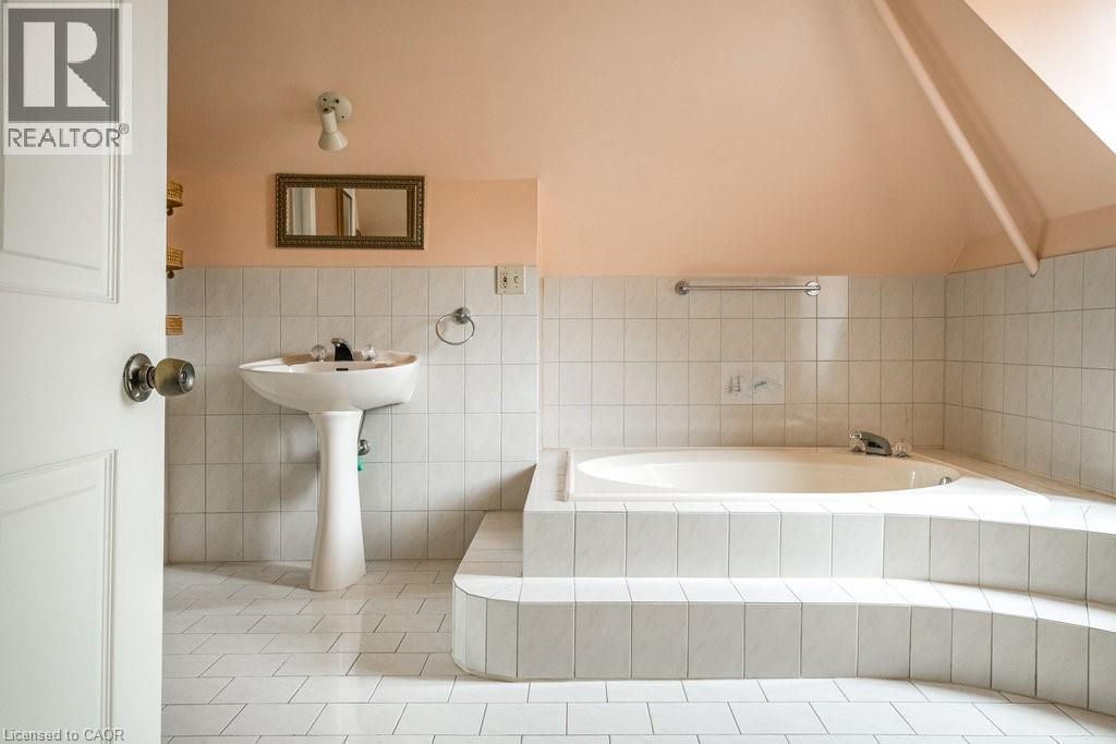 Bathroom featuring a pedestal sink, white tiled flooring, and a built-in bathtub surrounded by white tile - 95-97 S Fairholt Road S, Hamilton, ON - Indoor Photo Showing Bathroom