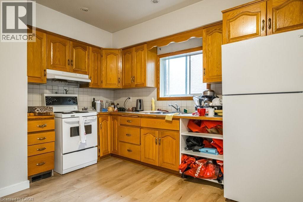 Kitchen featuring wood cabinetry, white appliances, a tiled backsplash, and wood-finish flooring - 95-97 S Fairholt Road S, Hamilton, ON - Indoor Photo Showing Kitchen