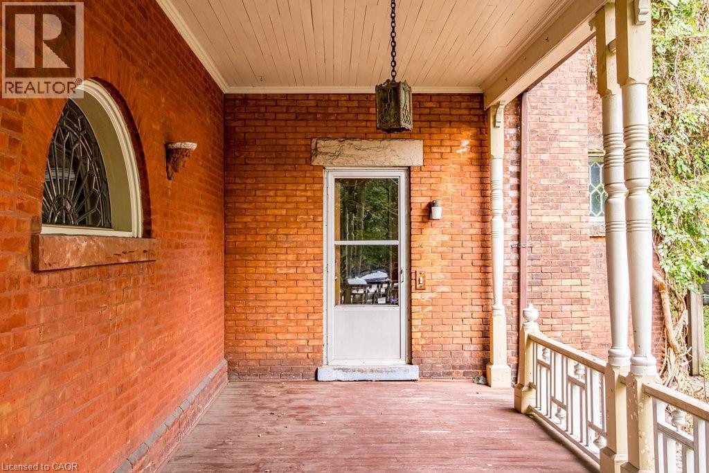 Brick exterior featuring a wooden porch, decorative balusters, and an arched window with leaded glass - 95-97 S Fairholt Road S, Hamilton, ON - Outdoor With Exterior