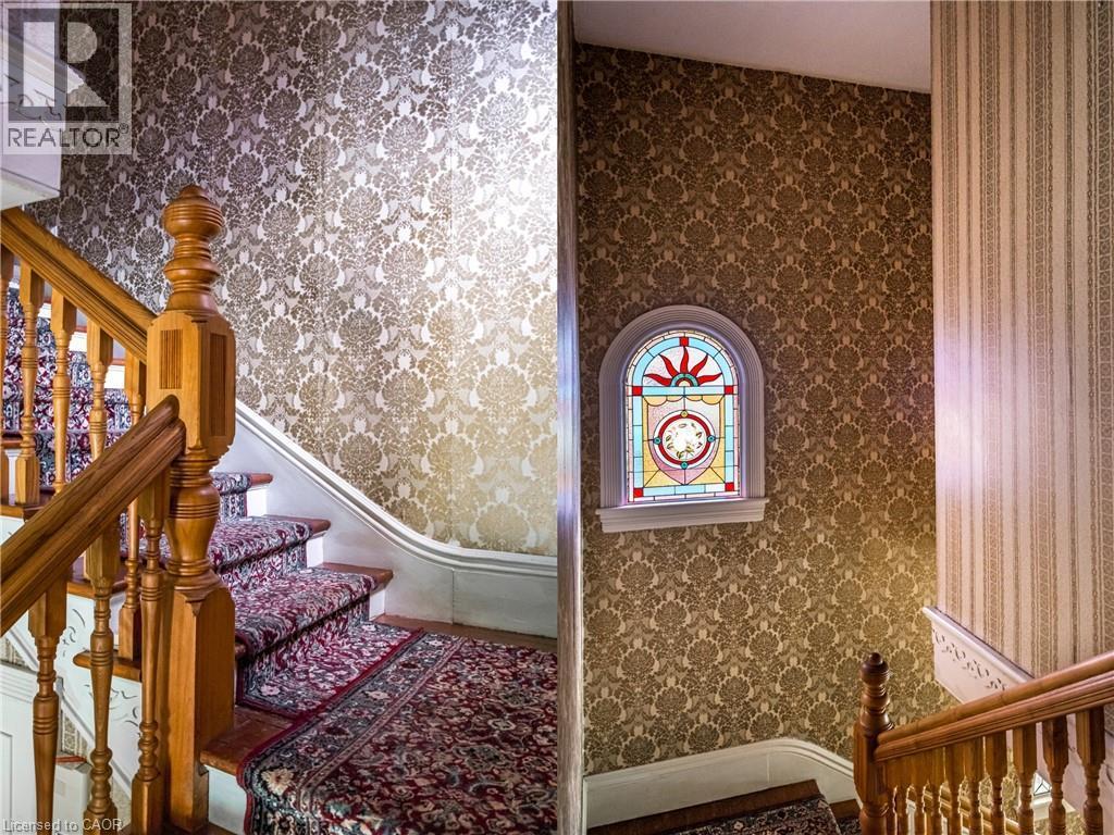 Curved staircase featuring wood balusters and a carpet runner, complemented by patterned wallpaper - 95-97 S Fairholt Road S, Hamilton, ON - Indoor Photo Showing Other Room