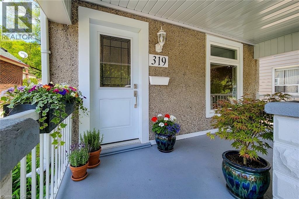Front porch entrance featuring a white door with leaded glass insert, textured stucco exterior, white trim, and a prominent house number - 319 King Street W, Dundas, ON - Outdoor With Exterior