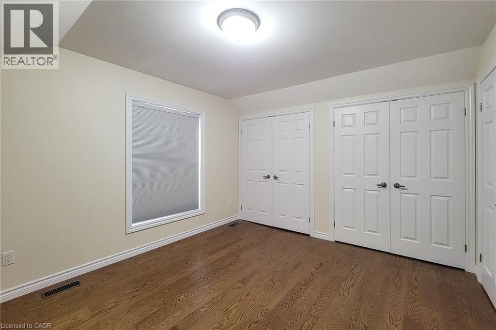Bedroom featuring wood-finish flooring, a window with roller shade, two bi-fold closet doors, and recessed lighting - 319 King Street W, Dundas, ON - Indoor Photo Showing Other Room