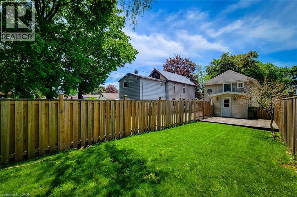 Expansive backyard featuring a manicured lawn, full privacy fencing, and a wooden deck - 319 King Street W, Dundas, ON - Outdoor
