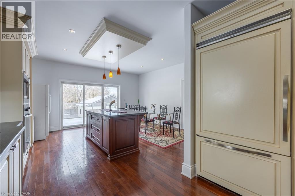 Spacious kitchen featuring a central island with integrated sink, rich wood-finish flooring, recessed lighting, and a custom panel-ready refrigerator - 514 Fishers Glen Road, Vittoria, ON - Indoor Photo Showing Kitchen