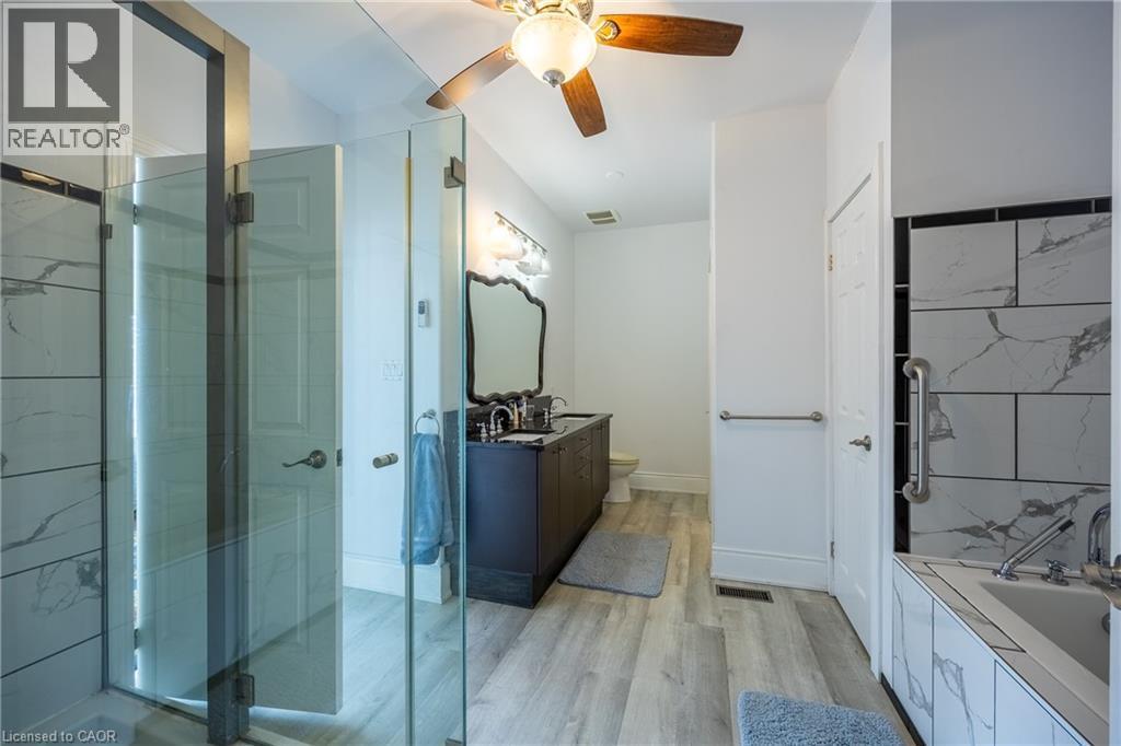 Bathroom featuring a glass-enclosed shower, a separate built-in bathtub with tiled surround, a dark wood-finish vanity with dual sinks, a decorative mirror, and wood-finish flooring - 514 Fishers Glen Road, Vittoria, ON - Indoor Photo Showing Bathroom