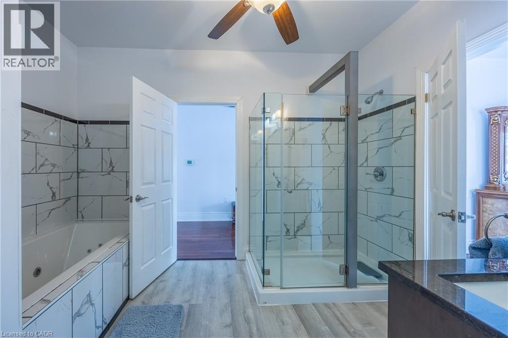 Contemporary bathroom featuring a glass-enclosed shower with tile surround, a built-in jetted tub with matching tile, wood-finish flooring, a ceiling fan, and a vanity with a dark countertop and integ - 514 Fishers Glen Road, Vittoria, ON - Indoor Photo Showing Bathroom