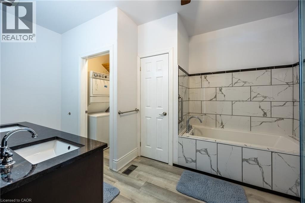 Bathroom featuring a built-in bathtub with subway tile surround, dark wood-finish vanity with an integrated sink and chrome faucet, and light wood-finish flooring - 514 Fishers Glen Road, Vittoria, ON - Indoor Photo Showing Bathroom