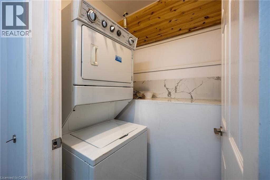 Dedicated laundry area with a stacked washer and dryer, wood-finish ceiling, and a white marble-patterned backsplash - 514 Fishers Glen Road, Vittoria, ON - Indoor Photo Showing Laundry Room