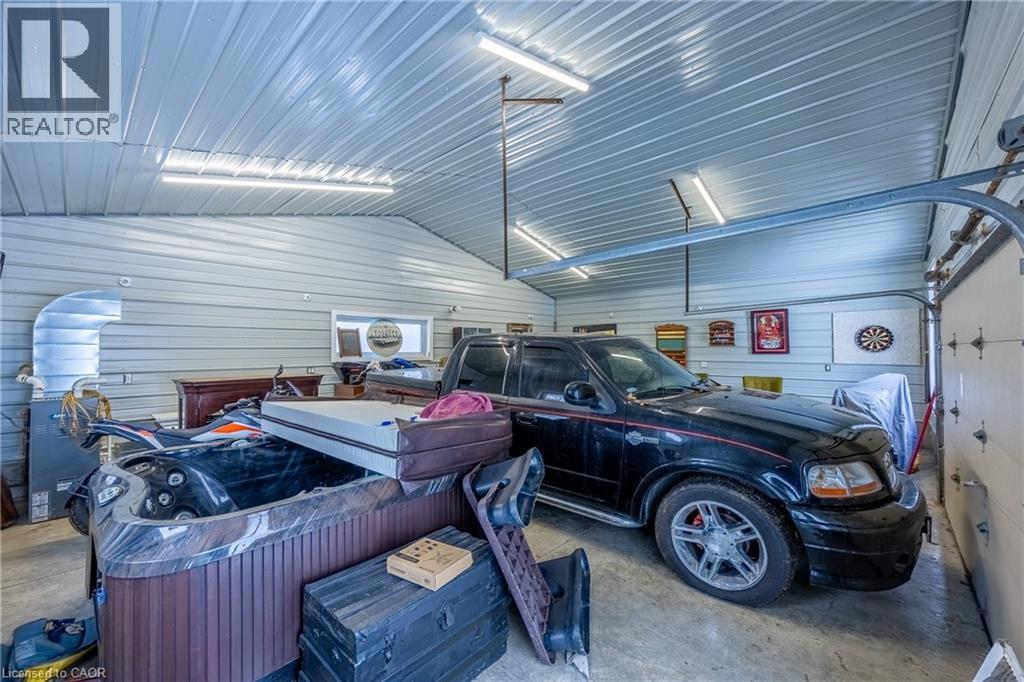 Spacious garage featuring a corrugated metal ceiling, metal-clad walls, multiple fluorescent light fixtures, and a large roll-up garage door with tracks - 514 Fishers Glen Road, Vittoria, ON - Indoor Photo Showing Garage