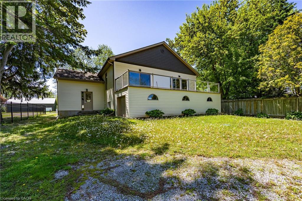 Rear elevation featuring a raised deck with glass railings, three arched basement windows, and beige siding - 514 Fishers Glen Road, Vittoria, ON - Outdoor