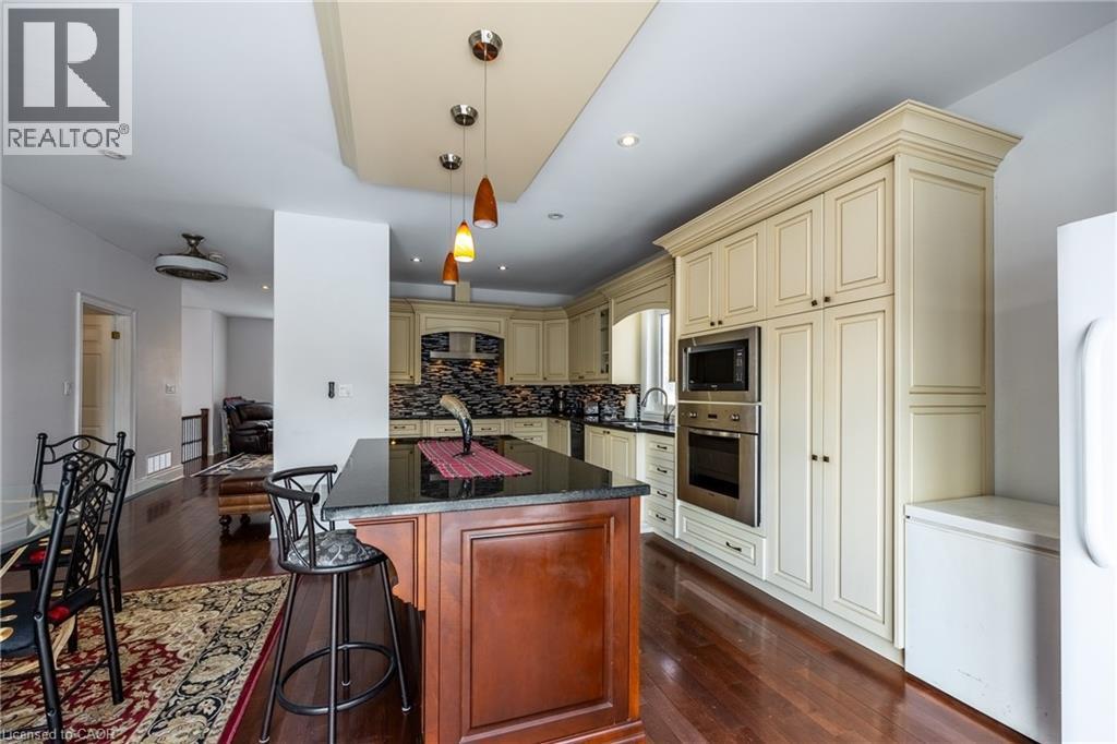 Gourmet kitchen featuring a wood-finish island with a black countertop, cream-toned cabinetry, built-in stainless steel appliances, and pendant lighting - 514 Fishers Glen Road, Vittoria, ON - Indoor Photo Showing Kitchen
