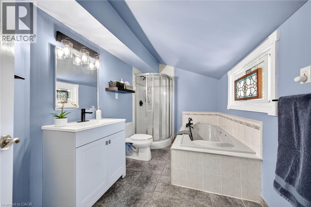 Bathroom featuring a white vanity with integrated sink, black fixtures, tiled flooring, a corner soaking tub, and a glass-enclosed shower - 439 Murray Street, Grimsby, ON - Indoor Photo Showing Bathroom