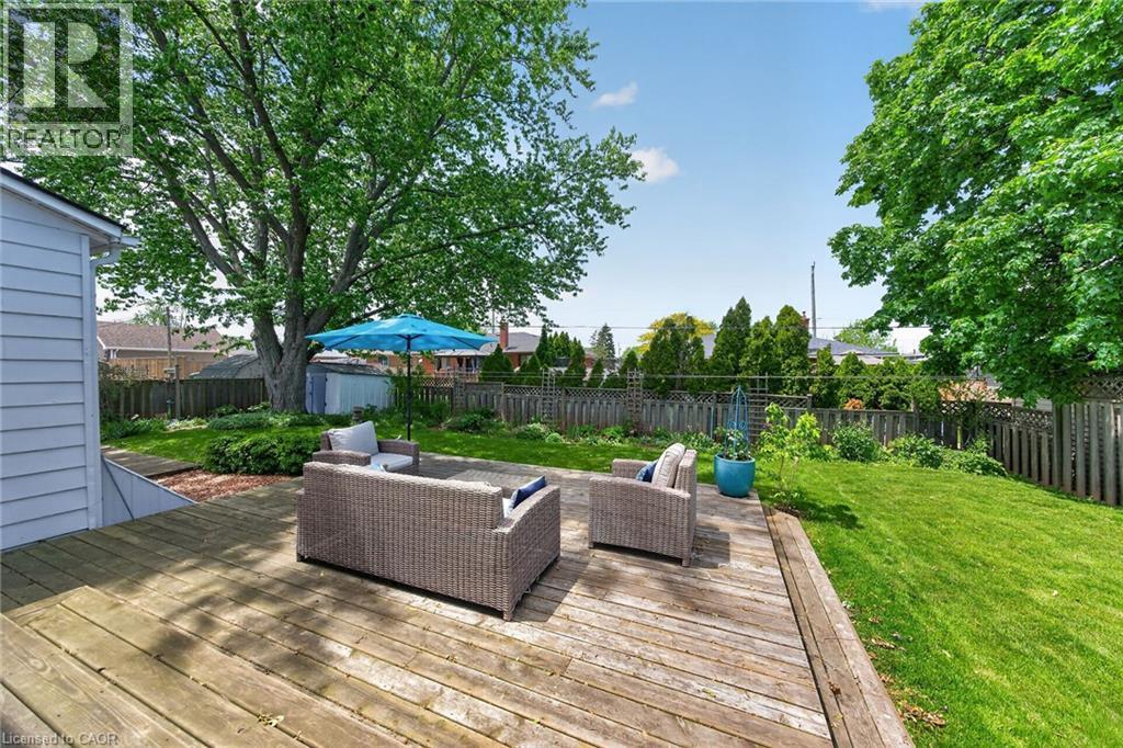 Expansive backyard featuring a large wooden deck, mature trees, a manicured lawn, and perimeter fencing - 439 Murray Street, Grimsby, ON - Outdoor With Deck Patio Veranda With Backyard