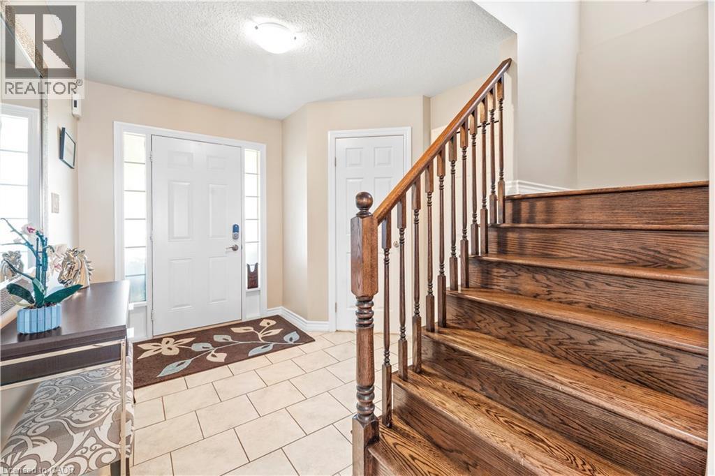 Entryway featuring a solid wood staircase with a turned baluster railing, a tiled floor, and a front door flanked by sidelight windows - 21 Davinci Boulevard, Hamilton, ON - Indoor Photo Showing Other Room