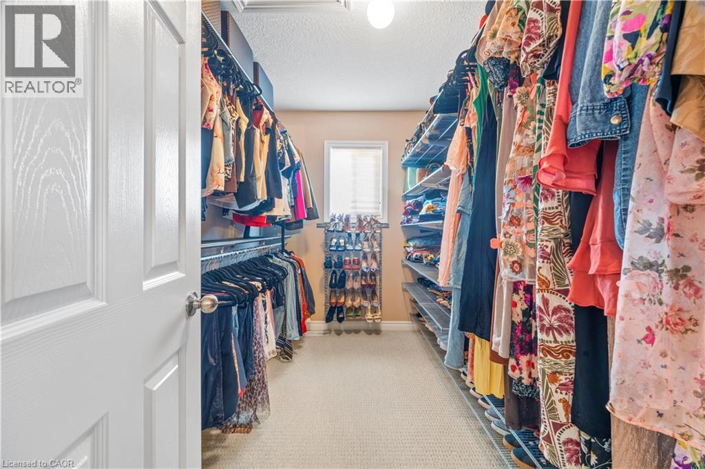 Walk-in closet featuring extensive built-in shelving, multiple hanging rods, neutral carpeting, and a single window with blinds - 21 Davinci Boulevard, Hamilton, ON - Indoor With Storage