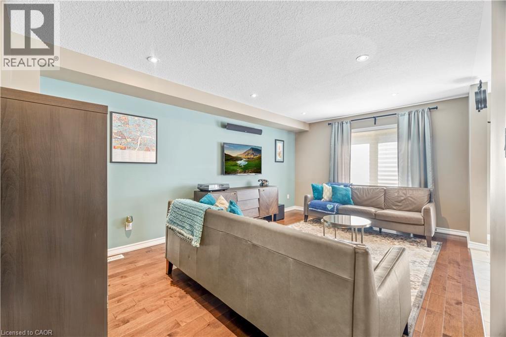 Living area with rich wood-finish flooring, recessed lighting, and a large window with horizontal blinds and drapery - 21 Davinci Boulevard, Hamilton, ON - Indoor Photo Showing Living Room