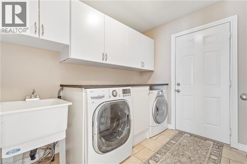 Dedicated laundry area featuring a utility sink, white upper cabinetry, and a dark countertop - 21 Davinci Boulevard, Hamilton, ON - Indoor Photo Showing Laundry Room