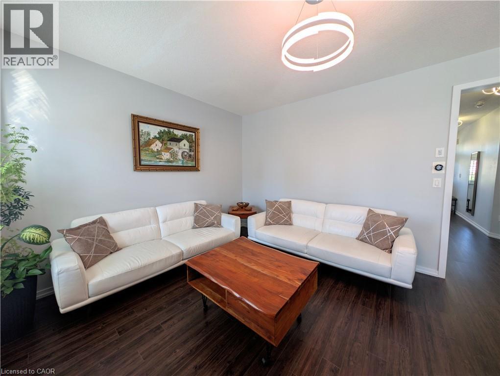 Spacious living area featuring dark wood-finish flooring, a contemporary circular pendant light fixture, and light-toned wall paint - 37 Mull Avenue, Caledonia, ON - Indoor Photo Showing Living Room