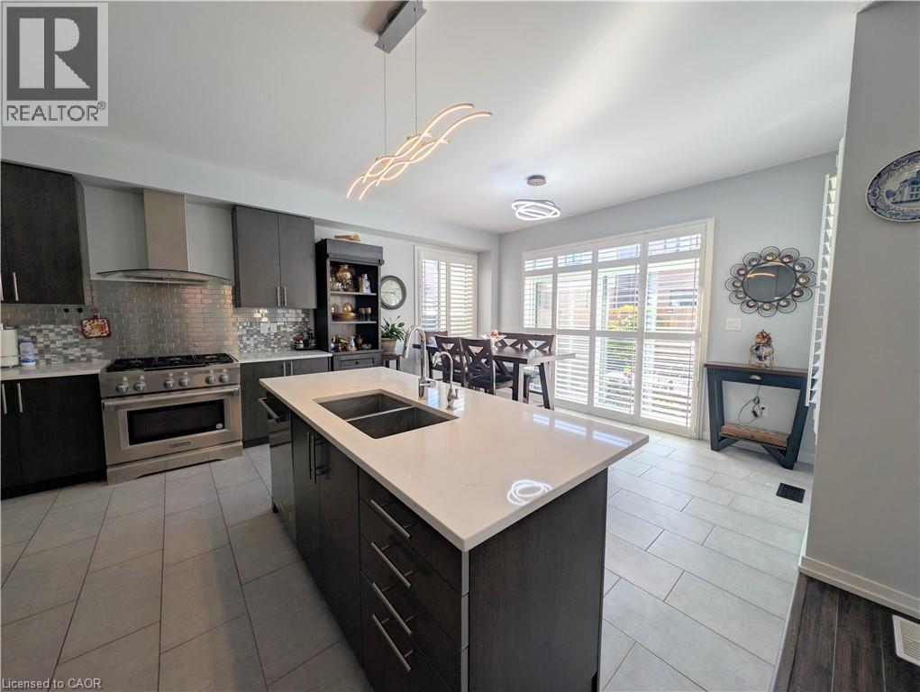 Modern kitchen featuring a spacious island with an undermount double sink, light-toned countertop, and dark wood-finish cabinetry - 37 Mull Avenue, Caledonia, ON - Indoor Photo Showing Kitchen With Double Sink With Upgraded Kitchen