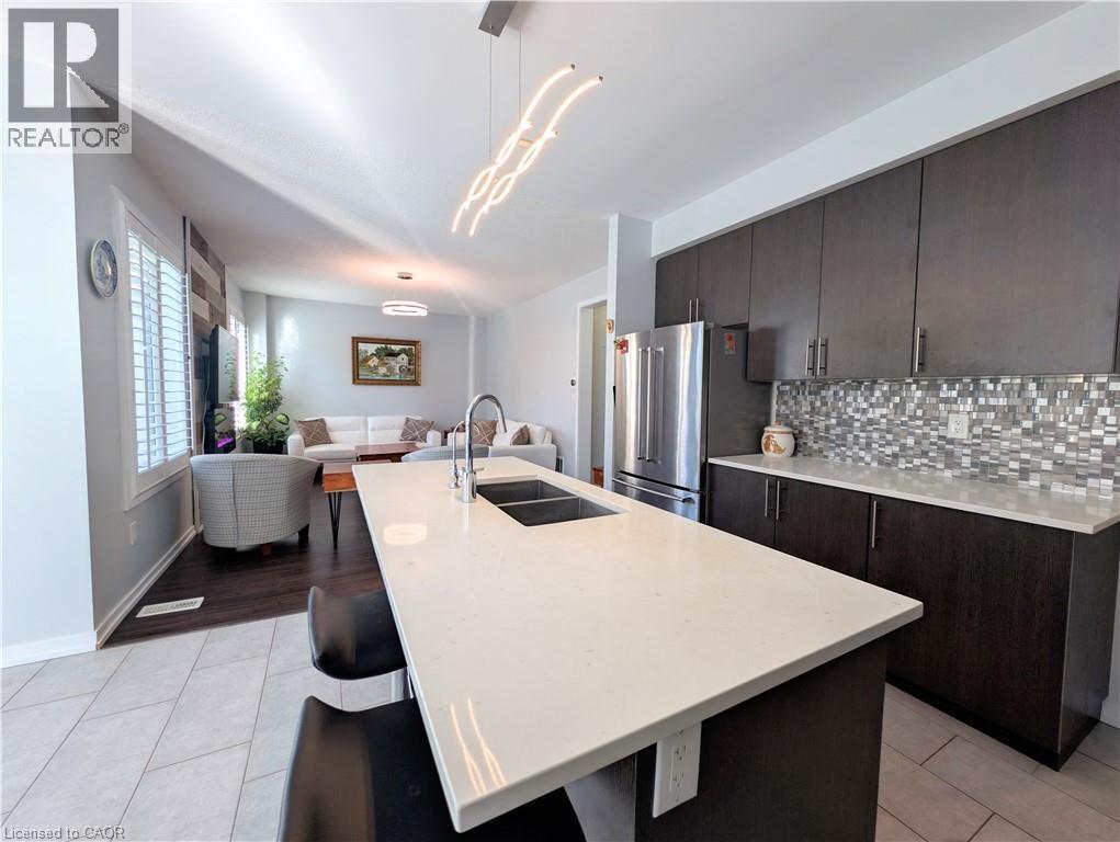 Kitchen island with dual basin sink, white countertop, and contemporary pendant lighting - 37 Mull Avenue, Caledonia, ON - Indoor Photo Showing Kitchen With Stainless Steel Kitchen With Double Sink With Upgraded Kitchen