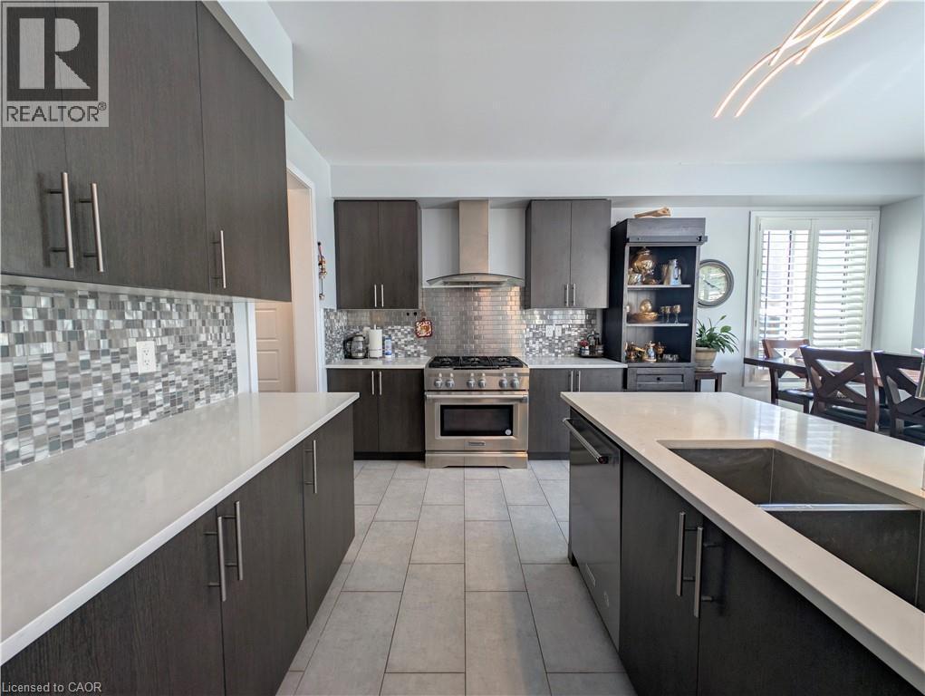 Contemporary kitchen featuring dark wood-finish cabinetry, light-toned countertops, a mosaic tile backsplash, stainless steel appliances, and a central island with an undermount sink - 37 Mull Avenue, Caledonia, ON - Indoor Photo Showing Kitchen With Double Sink With Upgraded Kitchen