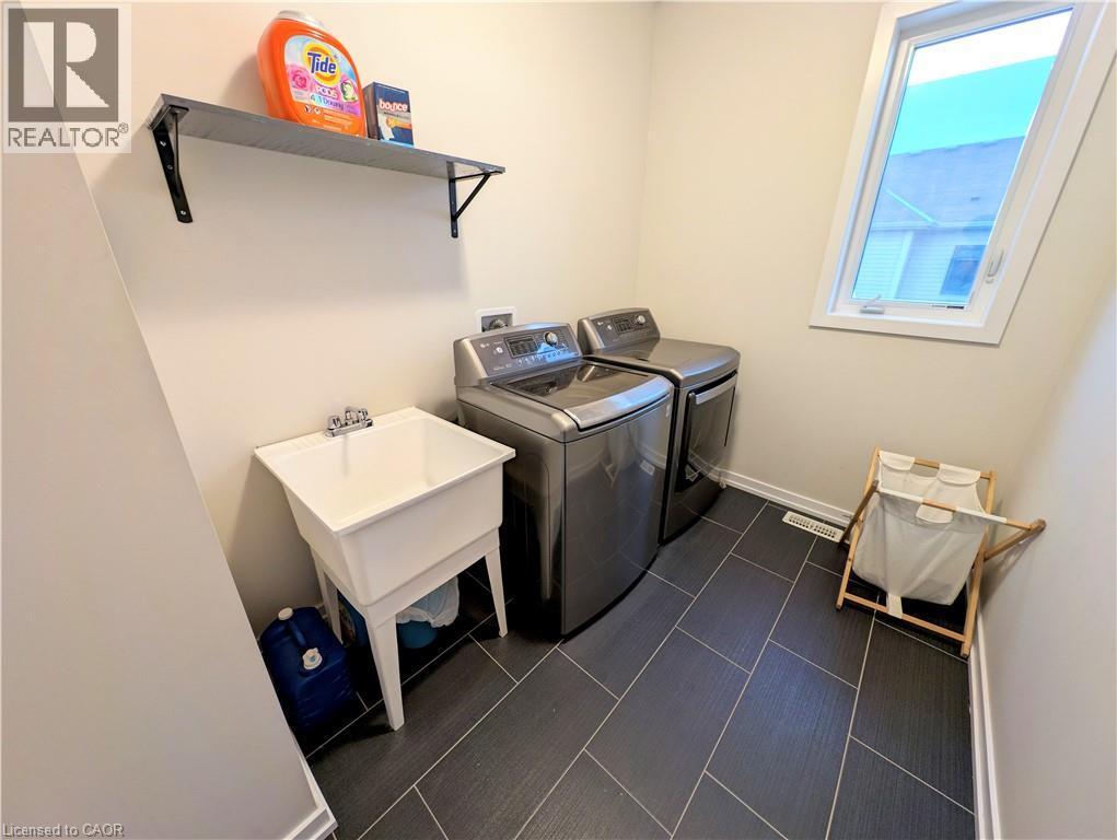 Functional laundry area featuring dark tile flooring, a utility sink, and a high-mounted window - 37 Mull Avenue, Caledonia, ON - Indoor Photo Showing Laundry Room