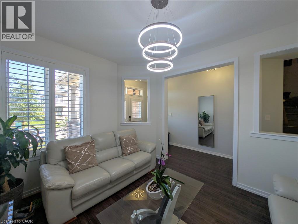 Living area featuring dark wood-finish flooring, white plantation shutters, and a three-tiered circular pendant light fixture - 37 Mull Avenue, Caledonia, ON - Indoor Photo Showing Living Room