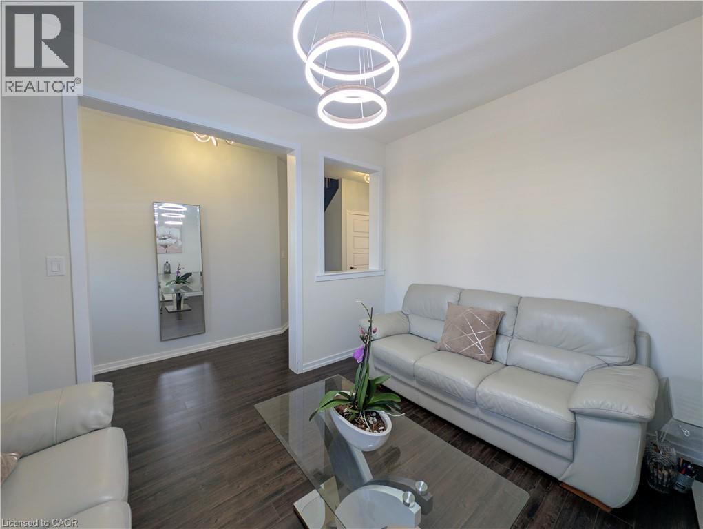 Living area featuring wood-finish flooring, a contemporary chandelier with circular rings, an open doorway, and a half-wall with a window-like opening - 37 Mull Avenue, Caledonia, ON - Indoor Photo Showing Living Room