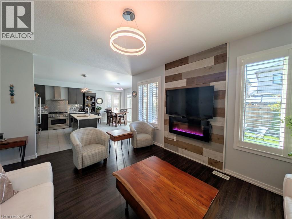 Open-concept living space featuring wood-finish flooring, a contemporary accent wall with an electric fireplace, and white plantation shutters - 37 Mull Avenue, Caledonia, ON - Indoor Photo Showing Living Room