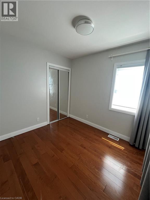 Room featuring wood-finish flooring, a window with natural light, and a mirrored closet - 179 S Vine Street S, St. Catharines, ON