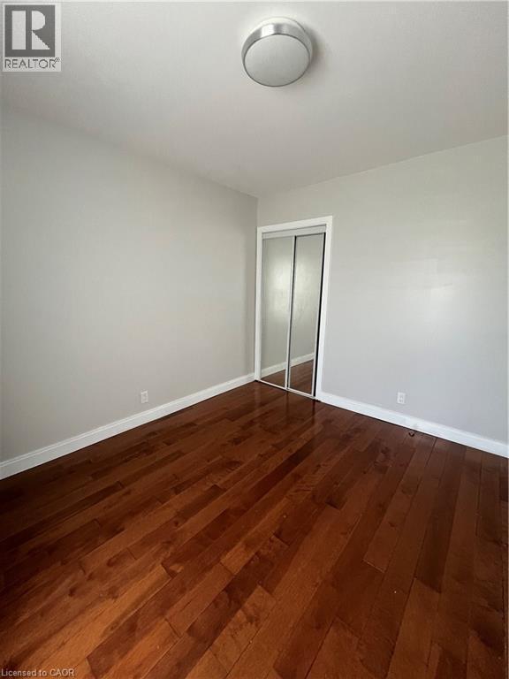Rich wood-finish flooring provides a warm foundation for this room, featuring light gray walls, white baseboards, and a semi-flush mount ceiling light - 179 S Vine Street S, St. Catharines, ON