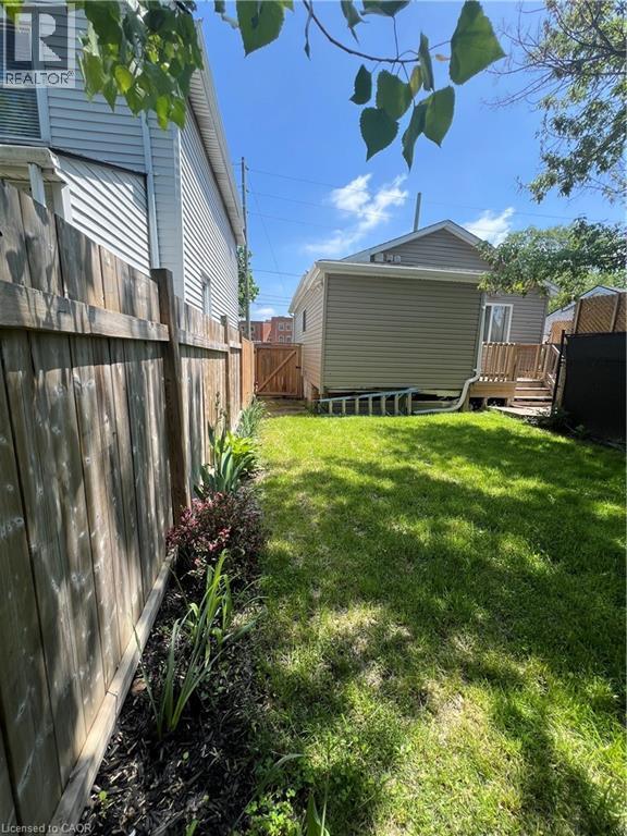 Fenced backyard featuring a manicured lawn, established garden bed, and a privacy fence leading to a rear gate - 179 S Vine Street S, St. Catharines, ON