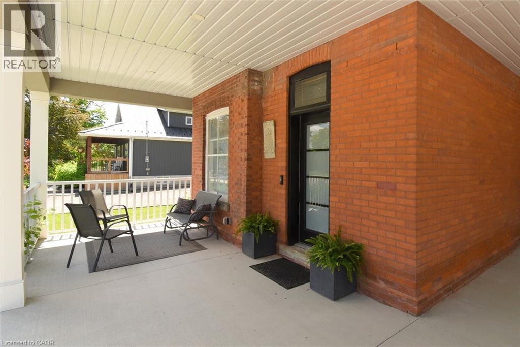 Expansive covered porch featuring a red brick facade and white railings. - 89 Lynden Road, Lynden, ON
