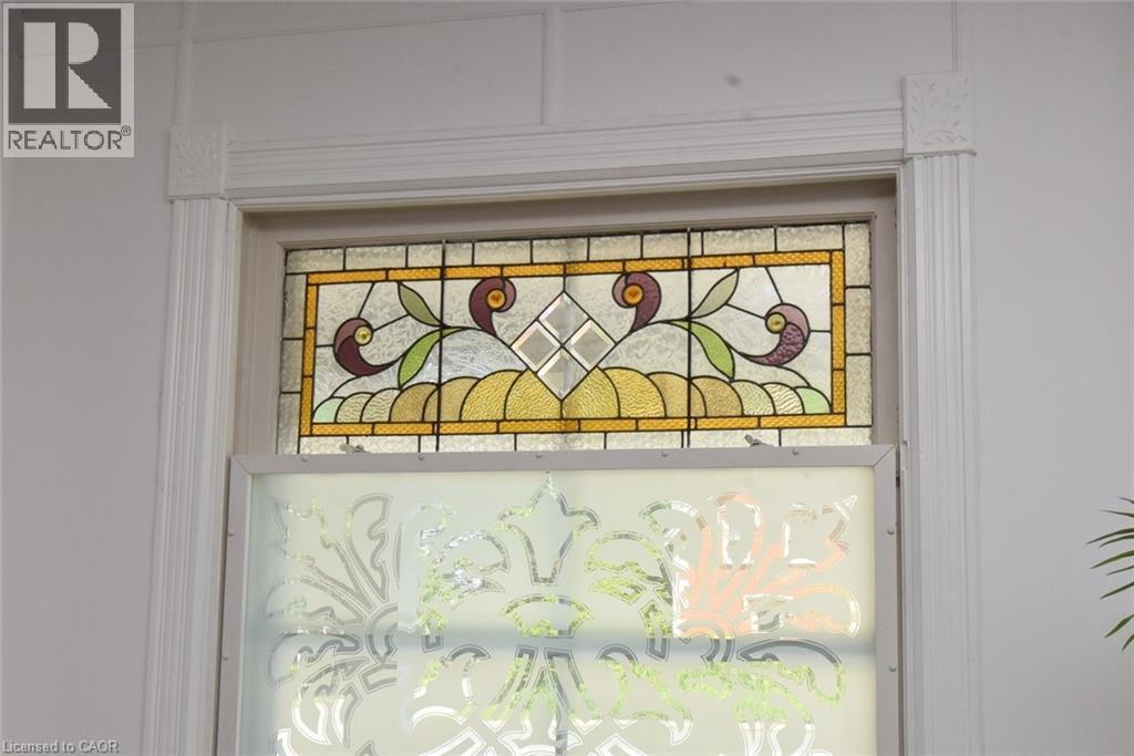 Window featuring an ornate stained glass transom and a frosted lower pane with a decorative pattern, framed by fluted trim and corner blocks - 89 Lynden Road, Lynden, ON