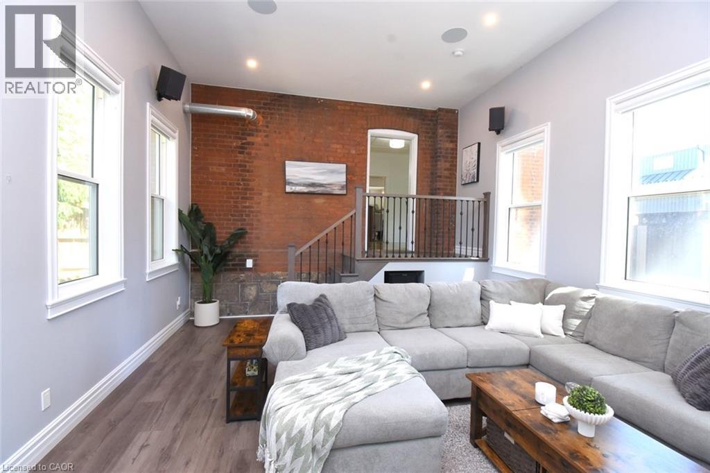 Family Room featuring an exposed brick wall, wood-finish flooring, recessed lighting, multiple windows, and an open stairwell with a dark wood railing - 89 Lynden Road, Lynden, ON