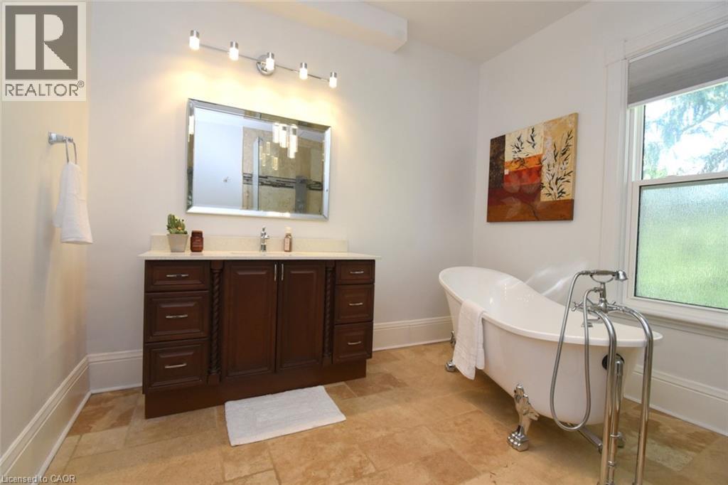 Bathroom featuring a freestanding clawfoot tub with a polished chrome faucet, a dark wood vanity with a white countertop, and a large framed mirror - 89 Lynden Road, Lynden, ON