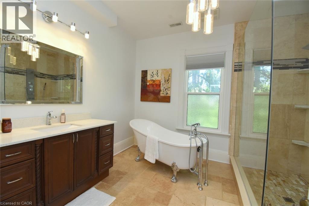 Bathroom featuring a freestanding clawfoot tub with a polished chrome faucet, a dark wood vanity with a white countertop, and a large framed mirror - 89 Lynden Road, Lynden, ON