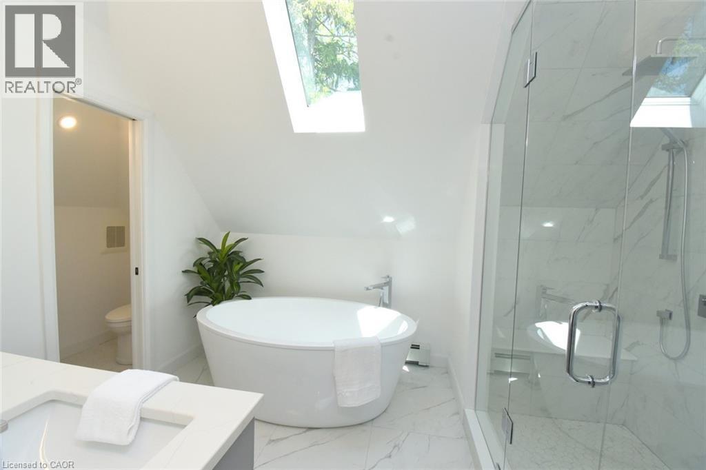 Modern bathroom featuring a water closet, freestanding soaking tub, a frameless glass shower with his and hers rain shower heads, double vanity, and skylight - 89 Lynden Road, Lynden, ON
